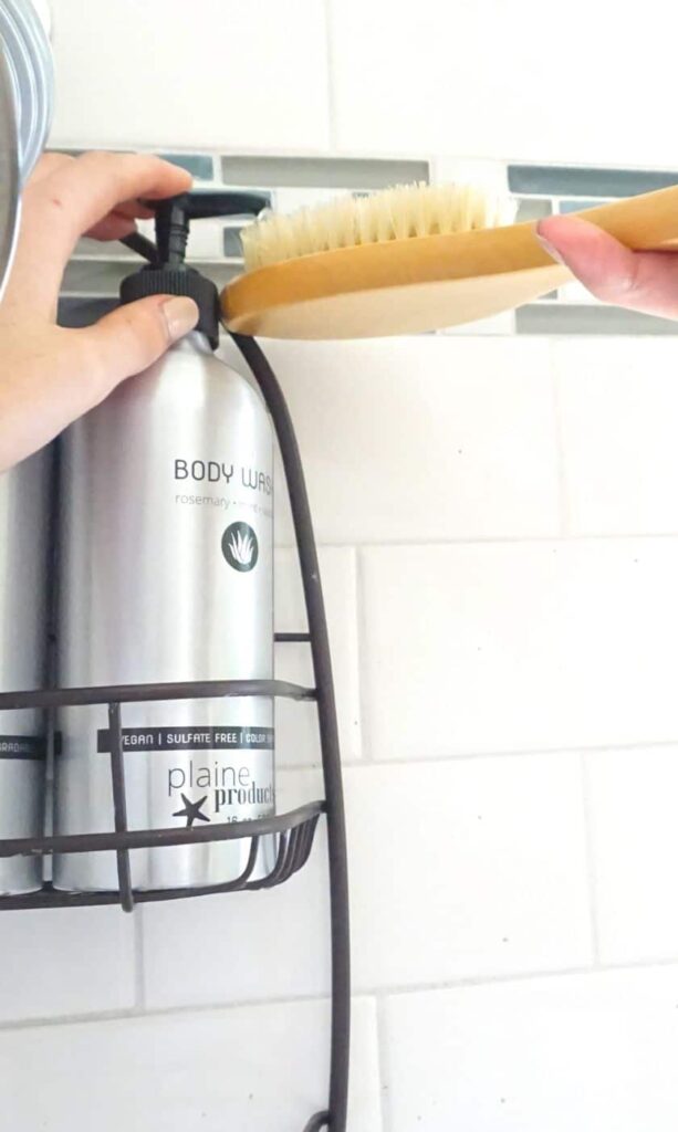a hand adding body wash to a bamboo scrub brush