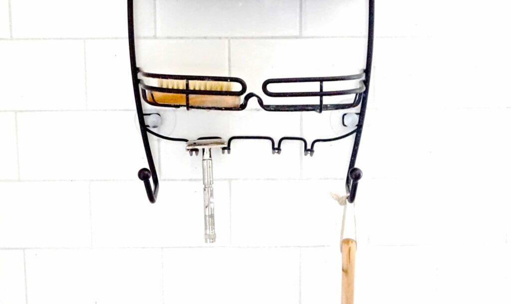 safety razor and scrub brush on a metal shower caddy