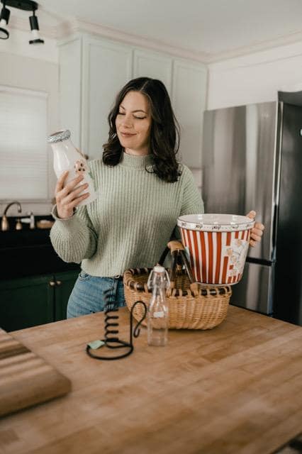 Woman holding a bottle with various thrifted gifts on the table
