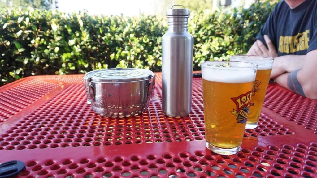 A tiffin, Kleen Kanteen, and two glasses of beer on a picnic table. 