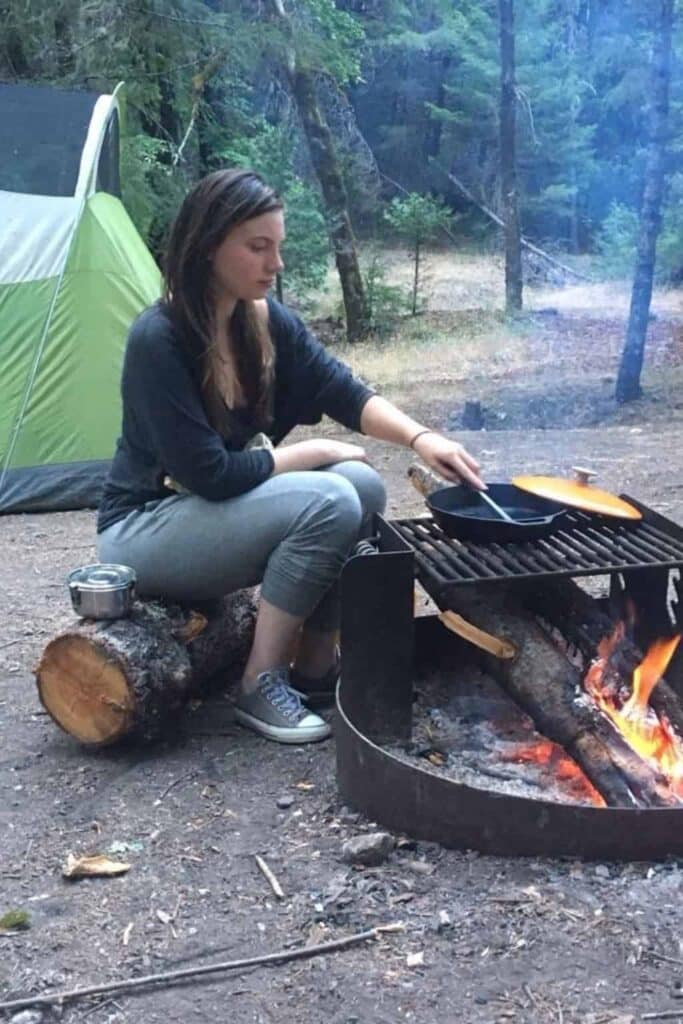A woman cooking over an open fire during a sustainable camping trip. 
