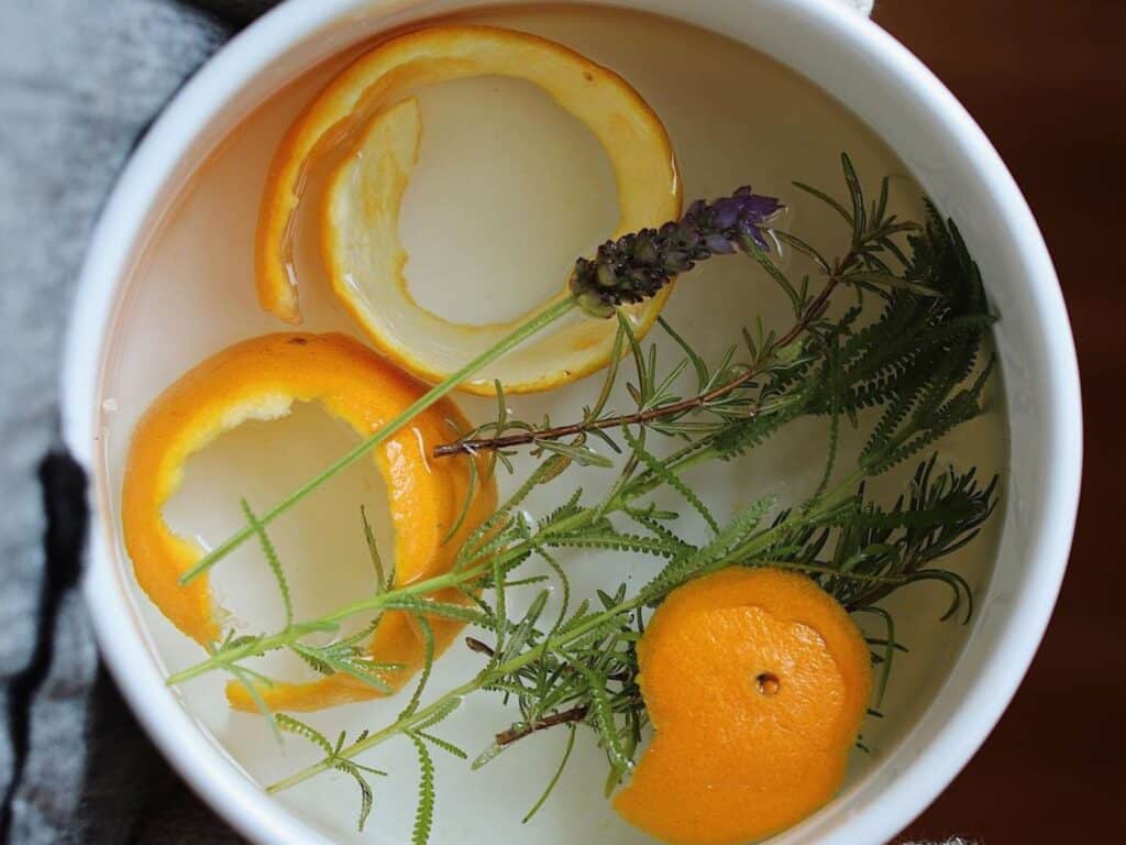 Simmering pot with orange peels and flower sprigs in simmering water.