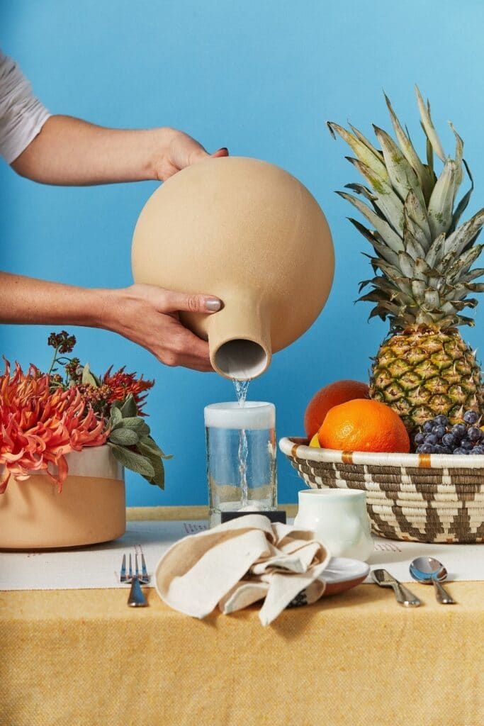 A brown water container pouring water into a glass to illustrate sites like Amazon that you can buy housewares from