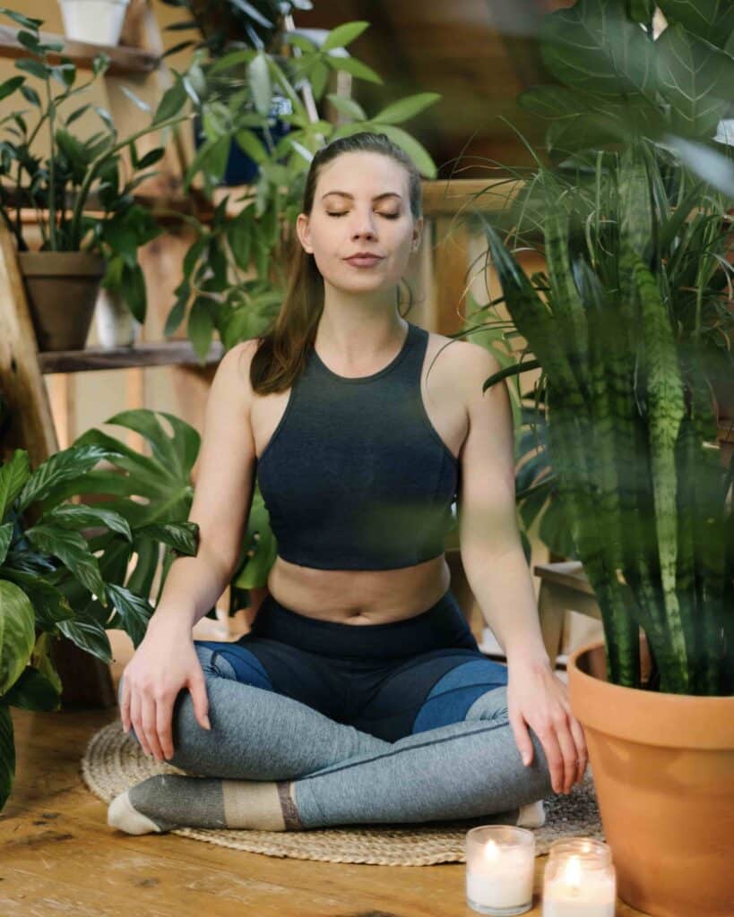 How to take care of yourself: a woman meditating next to her houseplants.