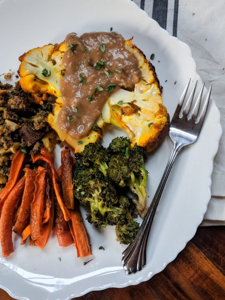 A cauliflower steak, roasted broccoli, and red bell peppers to illustrate vegan dinner recipes for two.