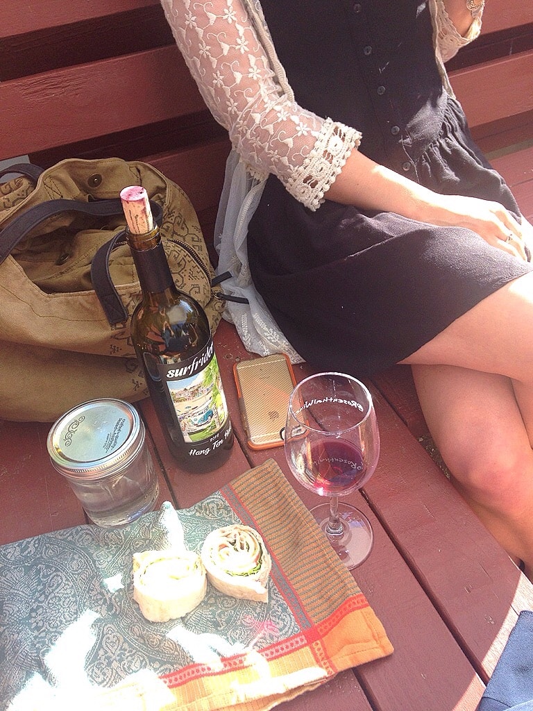 Eco friendly travel - A woman sitting on a bench with a bottle of wine, a mason jar, and a reusable napkin.